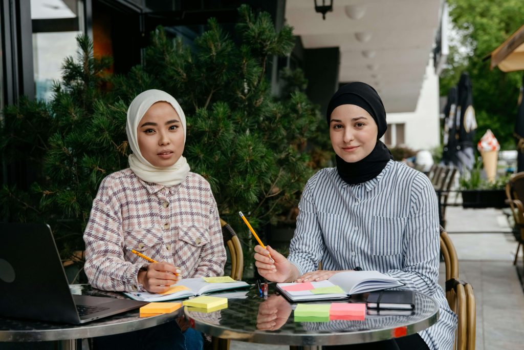 Two women wearing burqas working remotely on laptops in a collaborative, inclusive space, representing remote work gender inclusivity in purpose-driven careers.